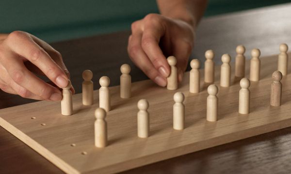 Hände mit Holzfiguren auf einem Systembrett