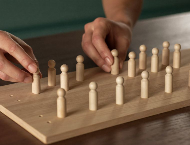 Hände platzieren Holzfiguren auf einem Systembrett